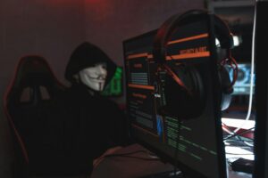 A person wearing a Guy Fawkes mask engaged in hacking activities on a computer in a dimly lit room.